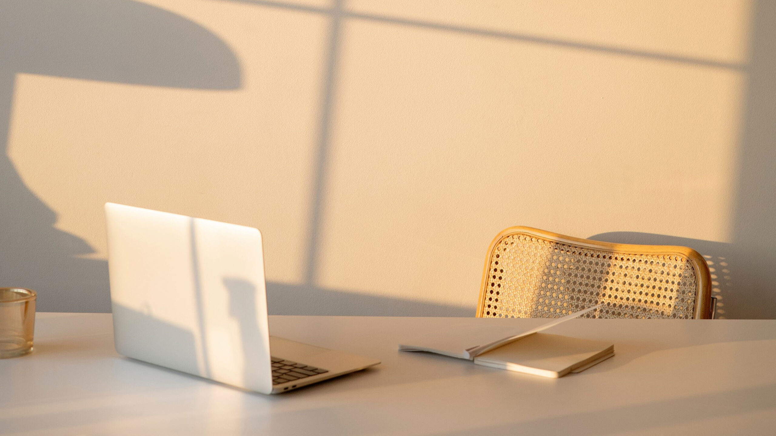 laptop and notebook on a clean desk at golden hour with shadows on the wall