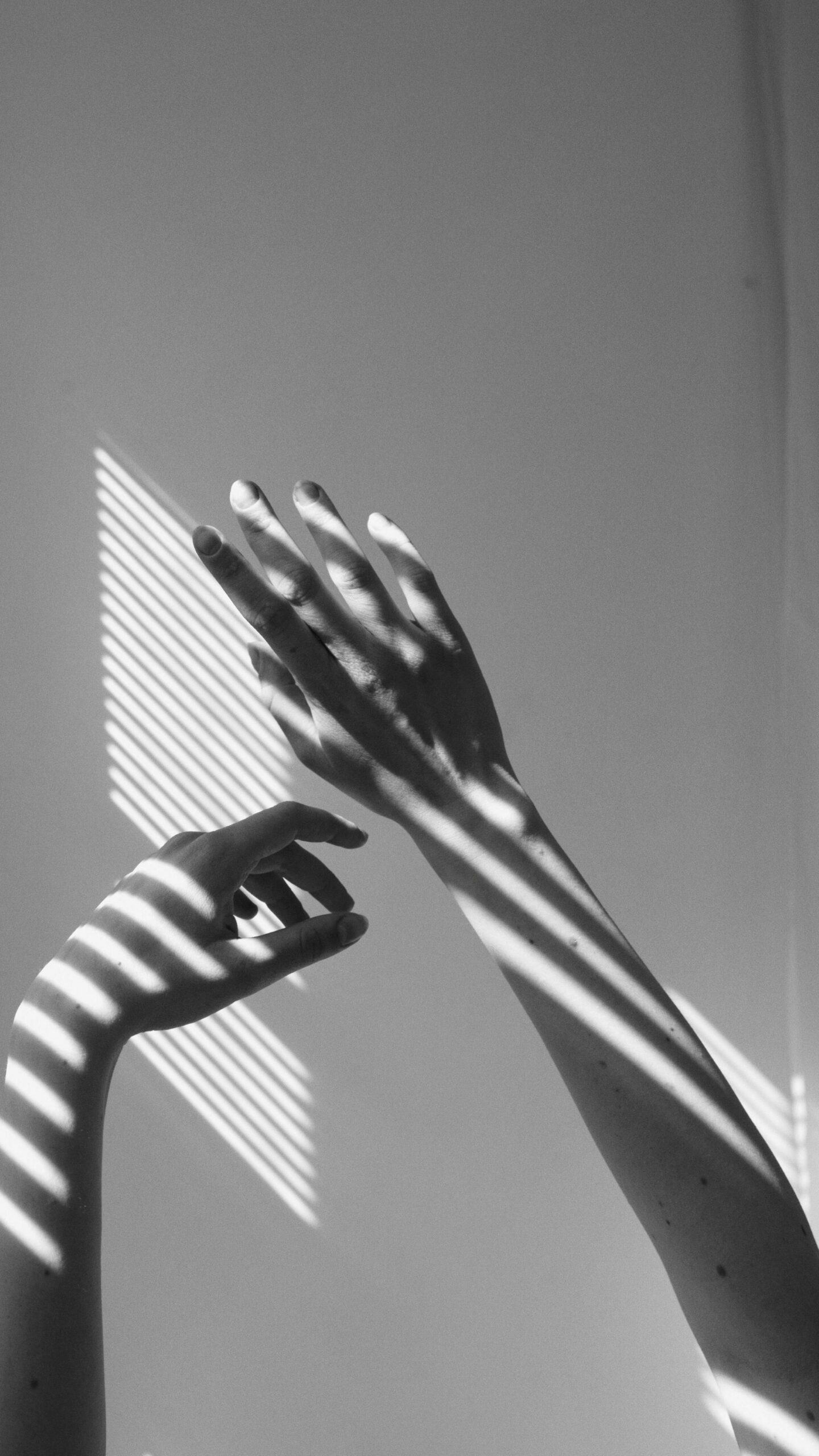 Grayscale photo of a person's hands with shadow of blinds across them
